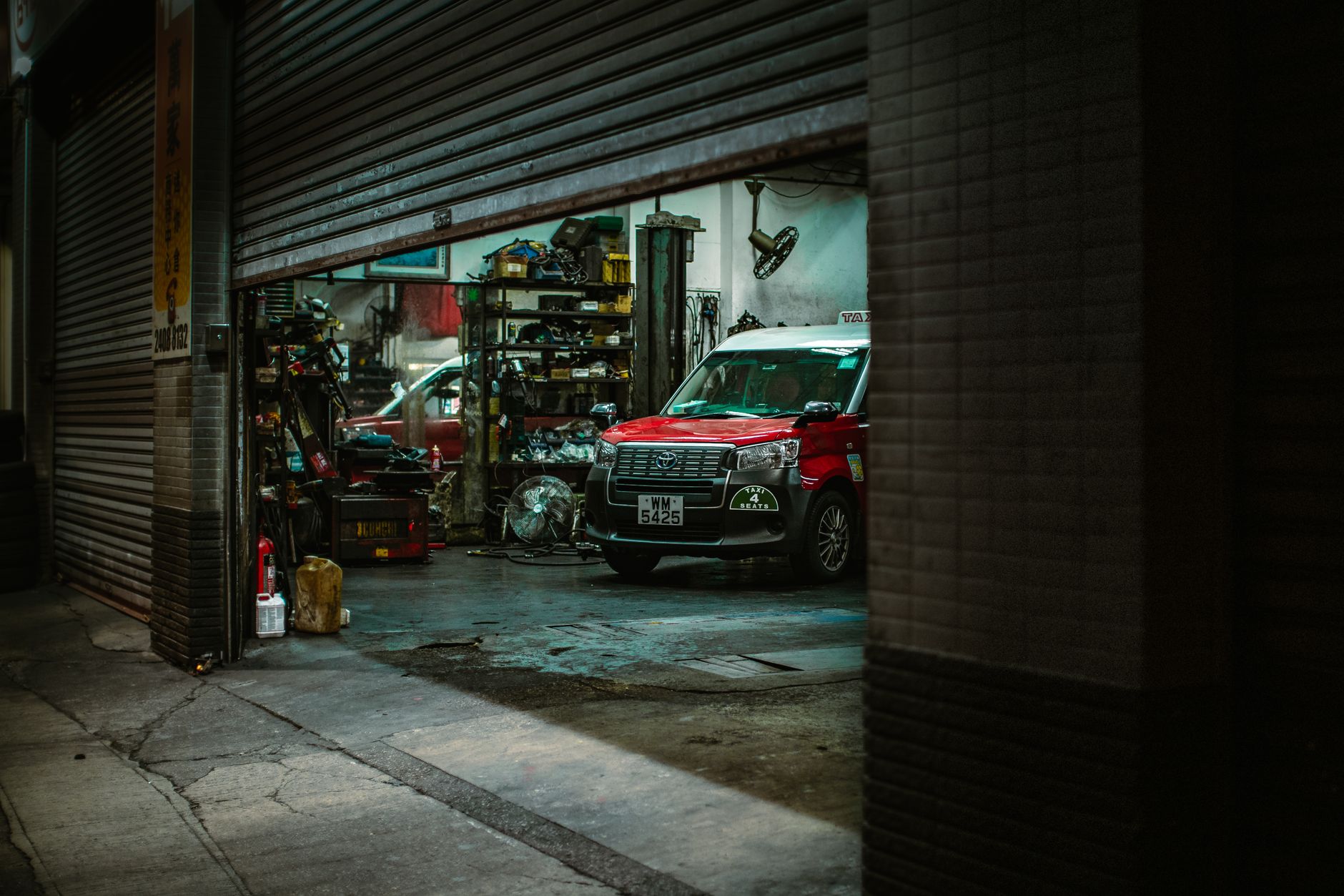 A red car inside a repair shop with the roller shutter open
