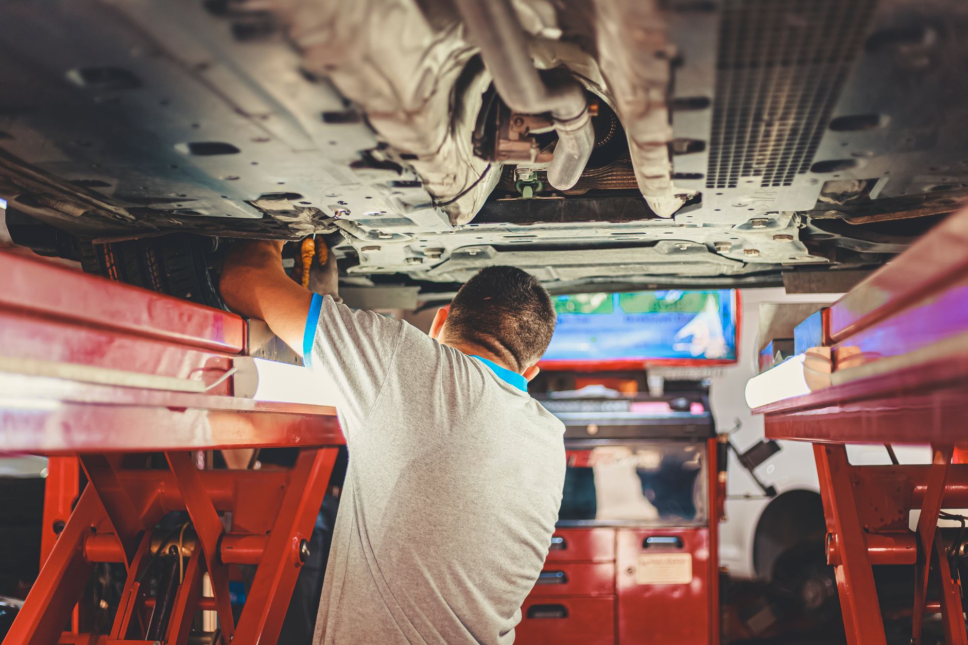 A mechanic in hi-vis working beneath a car raised on a lift in the repair bay