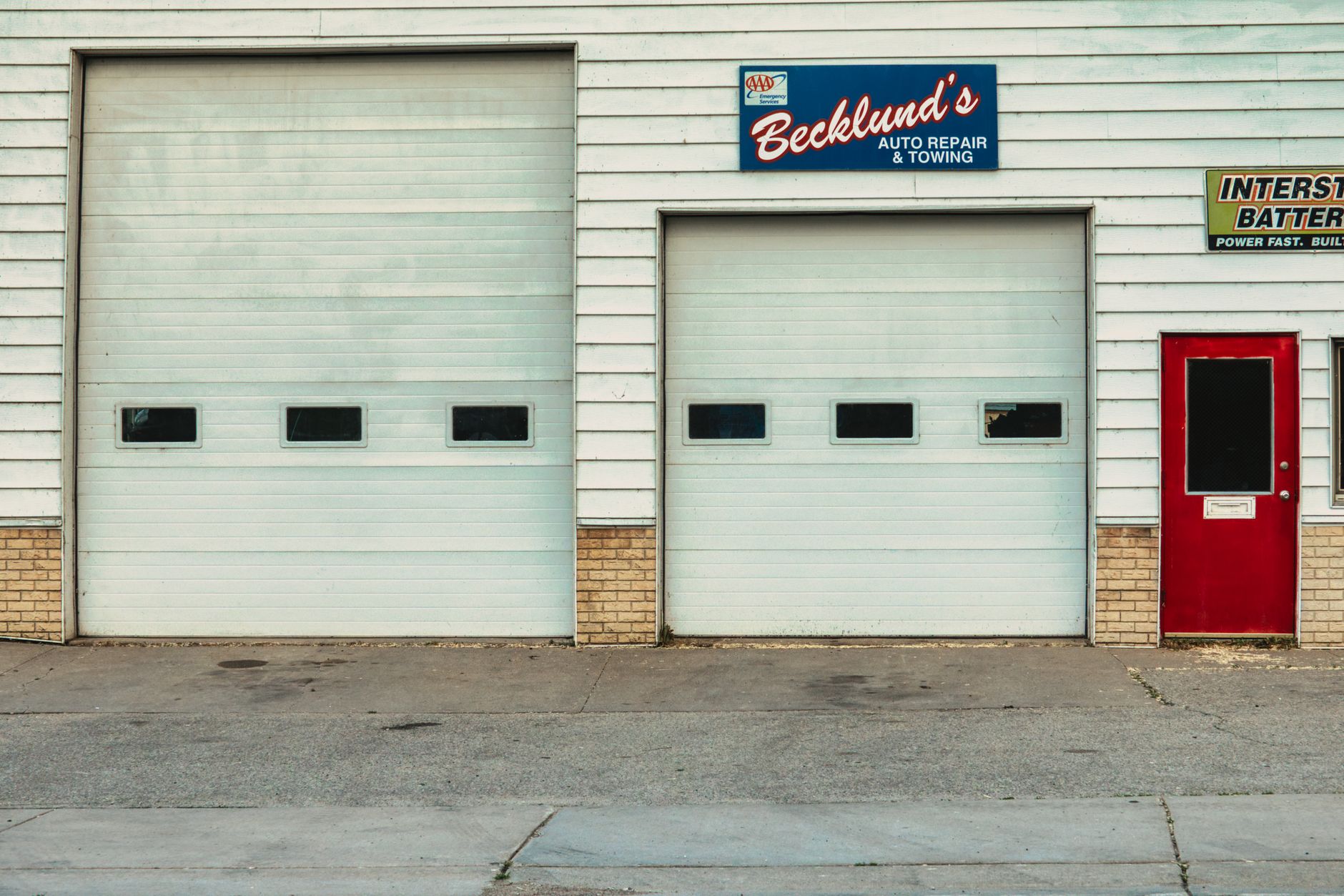 The front of an auto repair shop with roll-up garage doors and signage